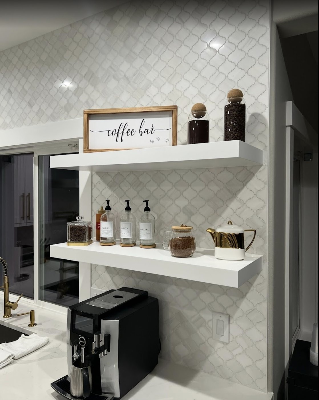 Arabesque mosaic tile backsplash behind white floating shelves at a kitchen coffee bar